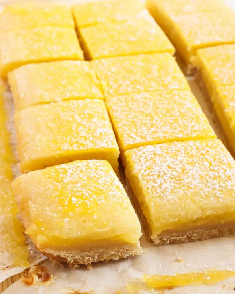 A close up view of a lemon square sprinkle with powdered sugar on parchment papper 