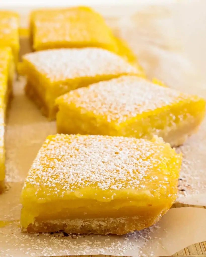 A close up view of a lemon square sprinkle with powdered sugar on parchment papper 