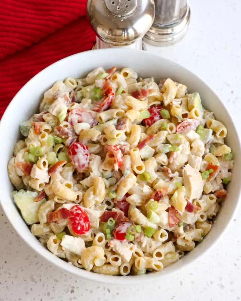 A large wide bowl with chicken pasta salad with tomatoes, green onions, and bacon. 
