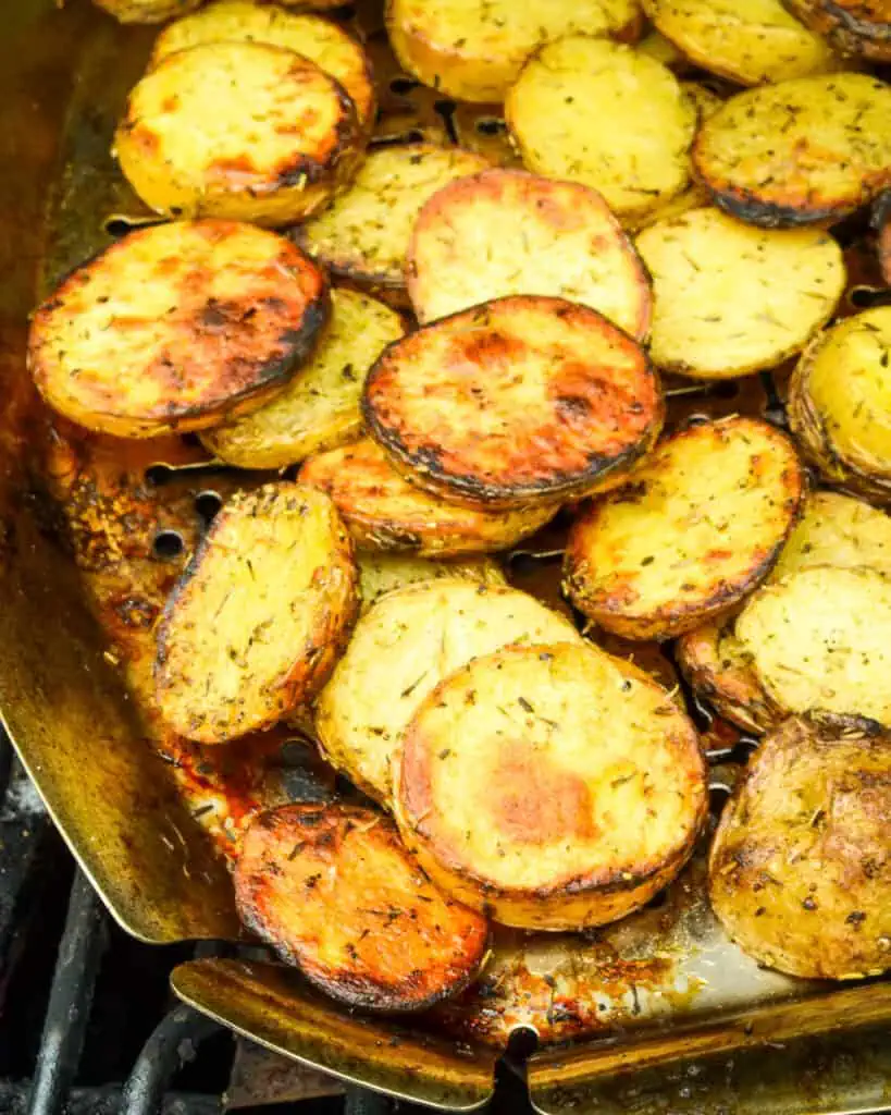 Grilled potatoes with herbs and seasonings in a grill basket on the grill. 