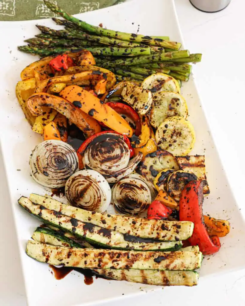 Assorted grilled vegetables on a white platter with a balsamic reduction sauce drizzled over them. 
