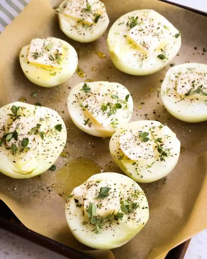 Cut yellow onions drizzled with olive oil and topped with a pat of butter and fresh herbs. 