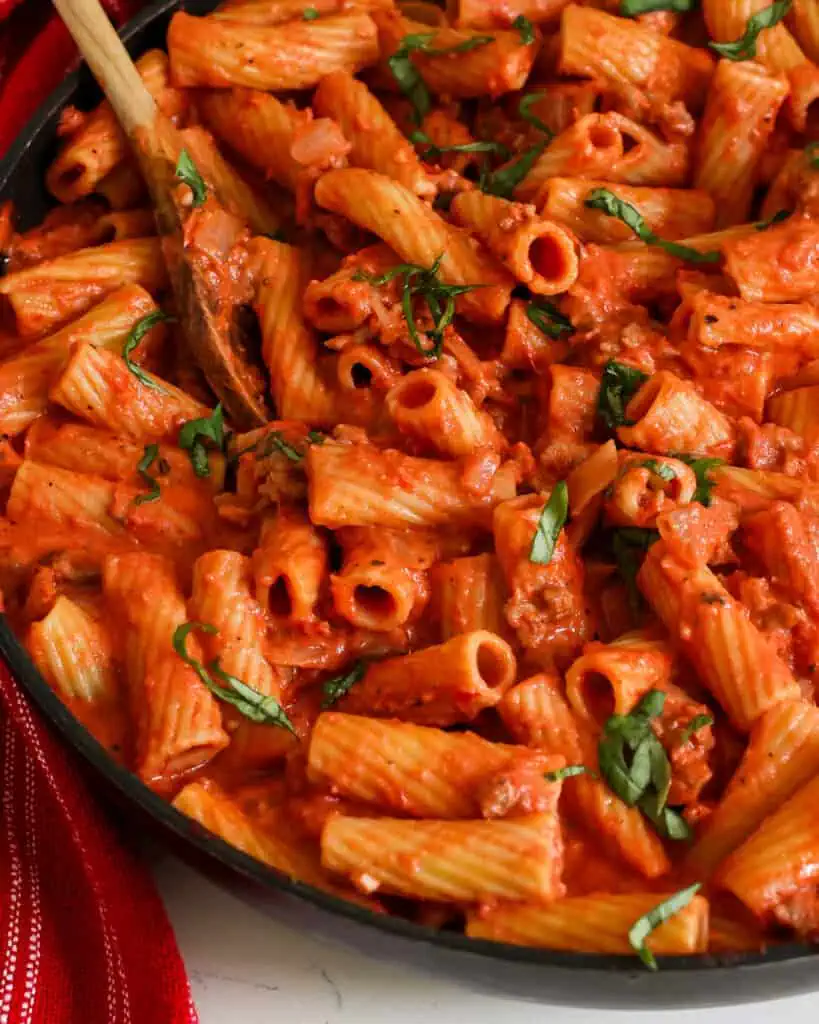 A close up view of susage rigatoni with homemade tomato sauce and basil ribbons. 