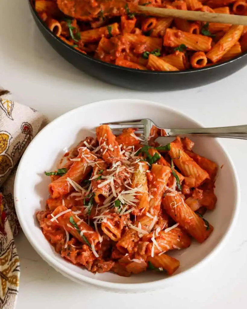 A bowl full of sausage rigatoni with freshly grated Parmesan cheese and
fresh basil ribbons. 
