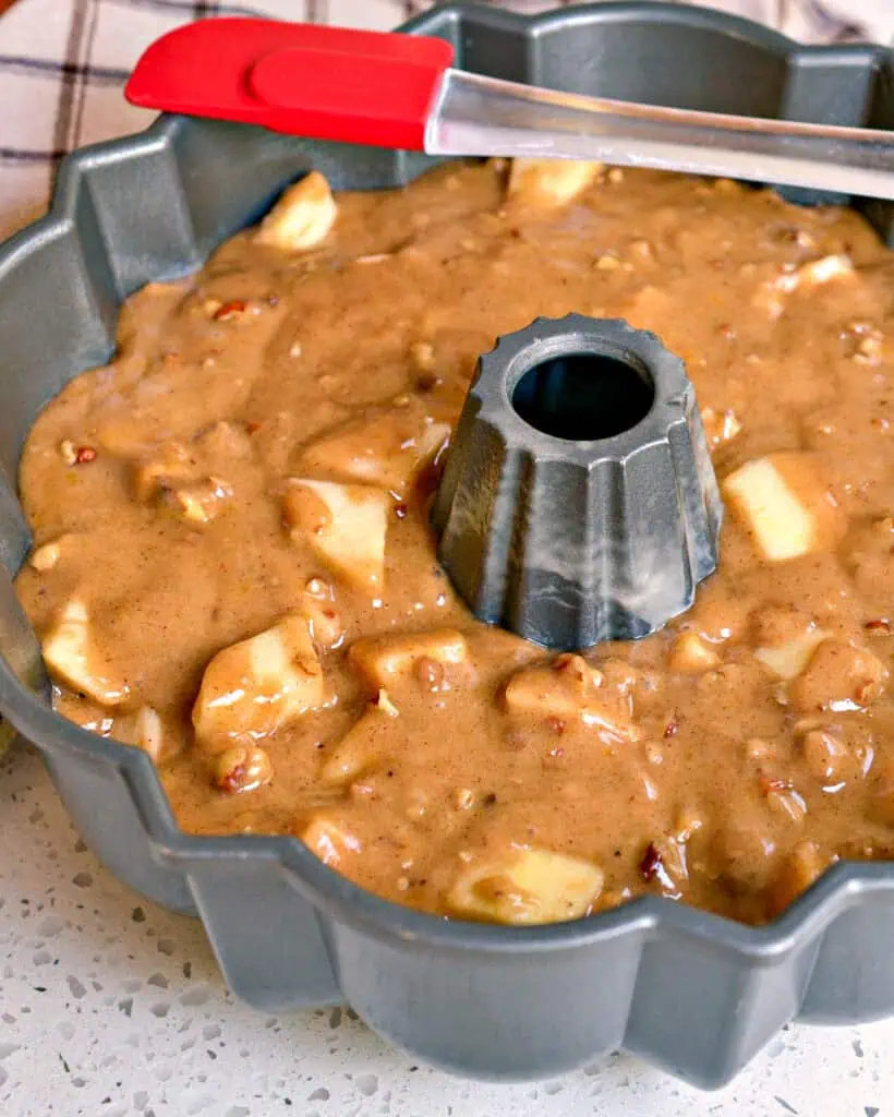 Apple cake batter in a bundt pan with a rubber spatula before being cooked. 