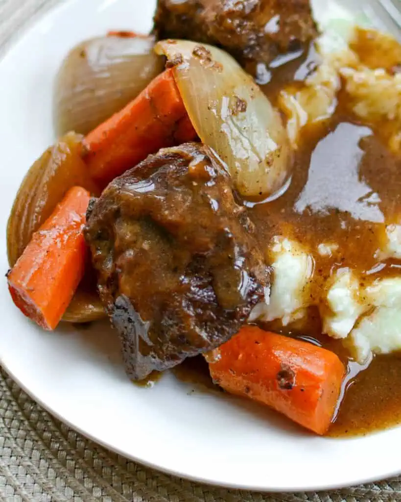 A plate full of fall off the bone beef short ribs with carrots, onions, and gravy. 