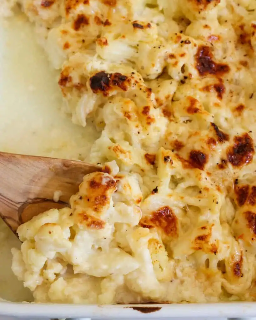 Cauliflower au gratin in a large casserole dish with a wooden spoon.