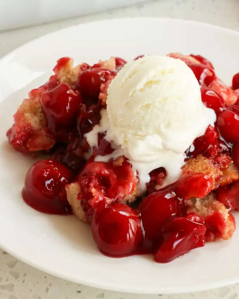 Cherry cobbler with a scoop of vanilla ice cream on a plate. 