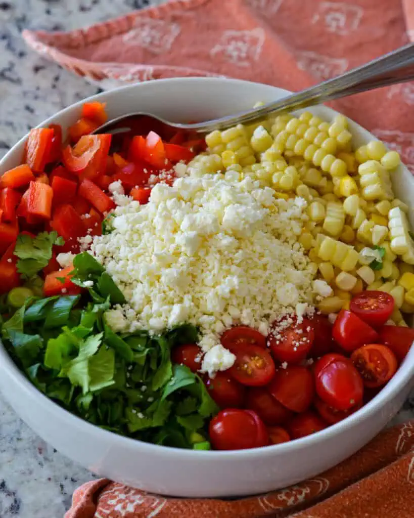 In a large bowl, add the cooked corn, diced red peppers, grape tomato halves, cilantro, green onions, minced jalapenos, feta, and red onion. Drizzle with the lime vinaigrette and toss to coat.