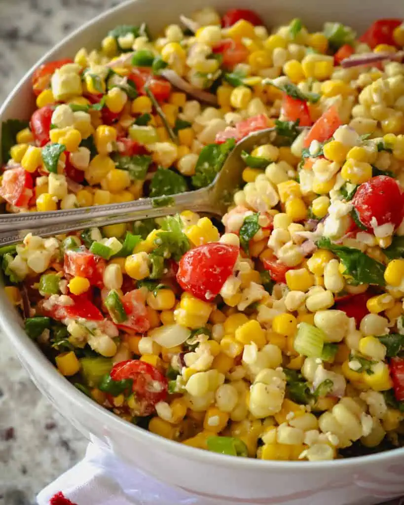 A bowl full of no mayo corn salad brings it all together with fresh corn, sweet red bell peppers, sun-ripened tomatoes, cilantro, minced jalapeno, chopped scallions, and feta cheese, all in a lightly sweetened lime vinaigrette.  