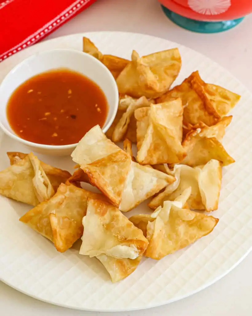 Cream cheese wontons on a plate with a small bowl of sweet and sour sauce. 
