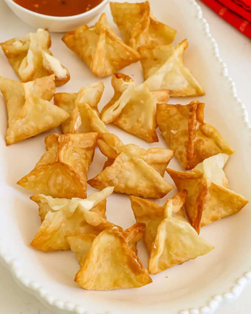 Cream cheese filled wontons on a serving platter with sweet and sour sauce. 