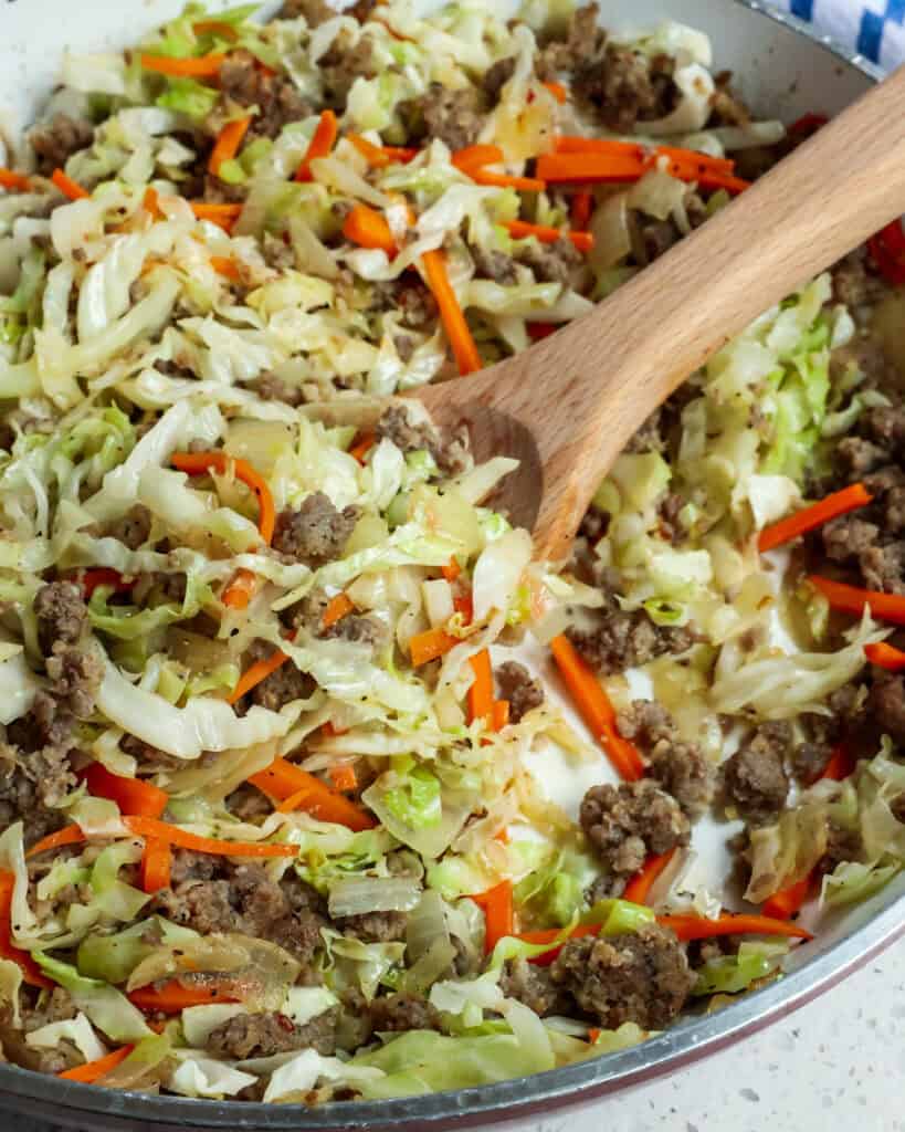 Sausage, onions, garlic, carrots,,and cabbage cooked up in a large skillet and stirred with a wooden spoon. 