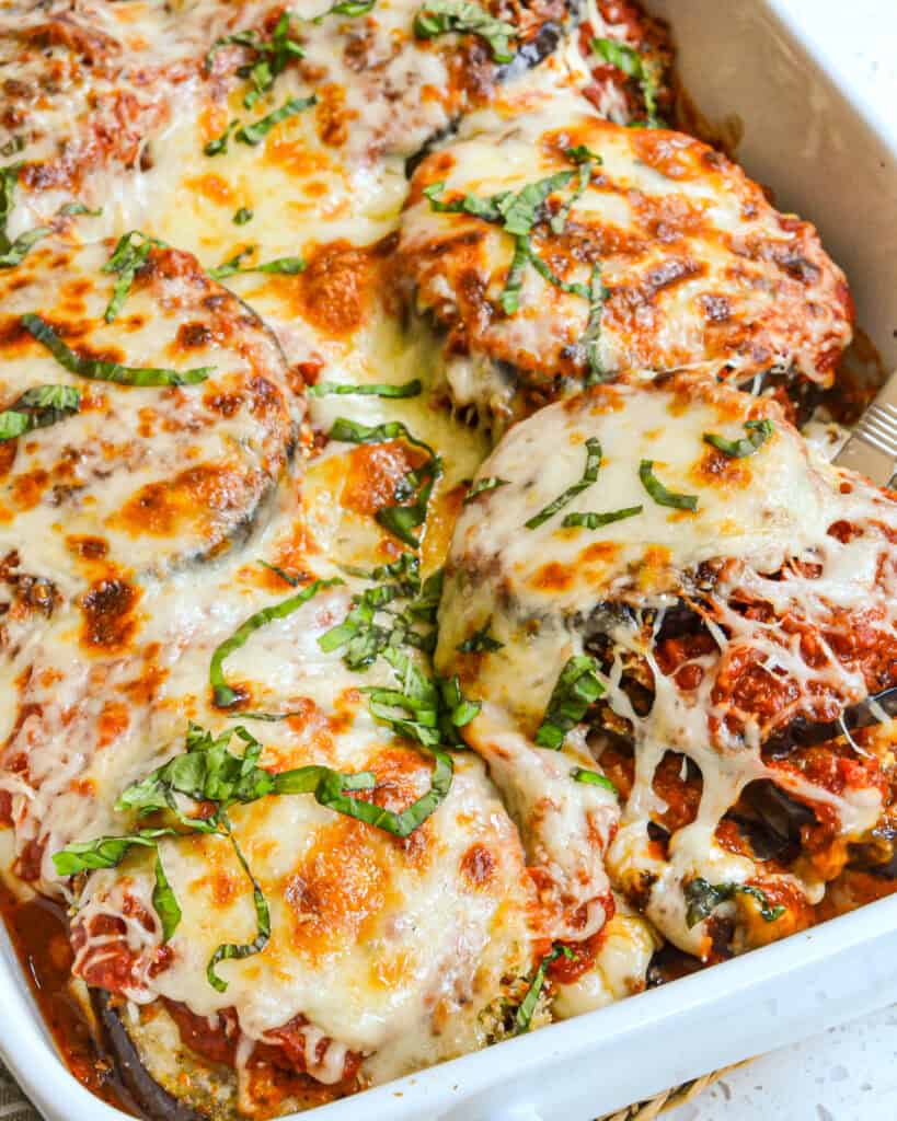 A casserole full of eggplant parmesan with a piece being removed with a spatula. 