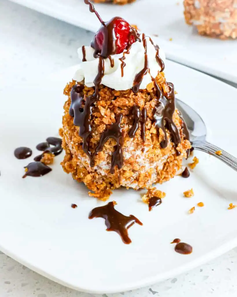 A scoop of fried ice cream topped with whipped cream and a cherry on an individual plate. 