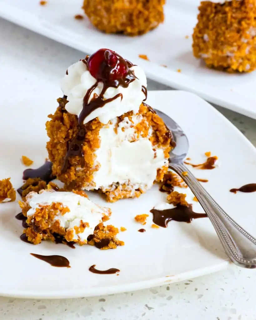 A scoop of no fry fried ice cream on plate with a bite missing and a spoon. 