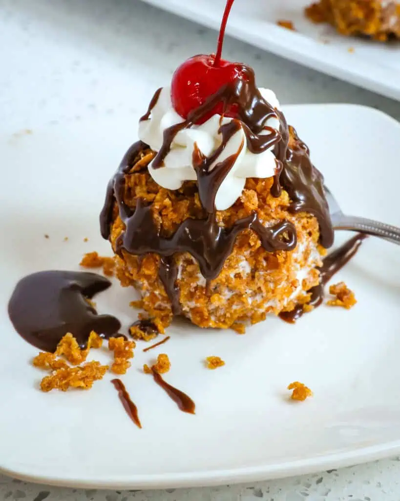 No fry Fried Ice Cream with a crispy cinnamon crunchy outer shell  drizzled with chocolate sauce, and topped with whipped cream and a cherry.  