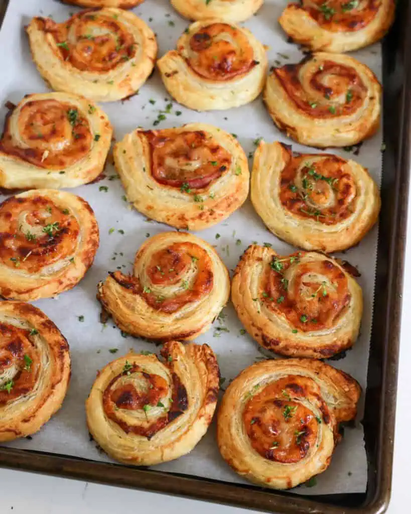 A baking sheet covred with parchment paper with ham and cheese pinwheels. 