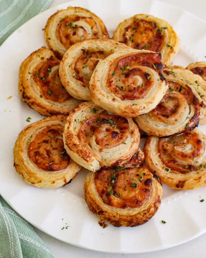 A large plate full of ham and cheese pinwheels made with puff pastry. 