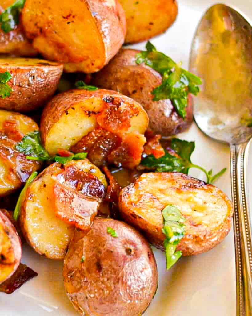 Warm honey bacon mustard potato salad on a platter with a large serving spoon. 