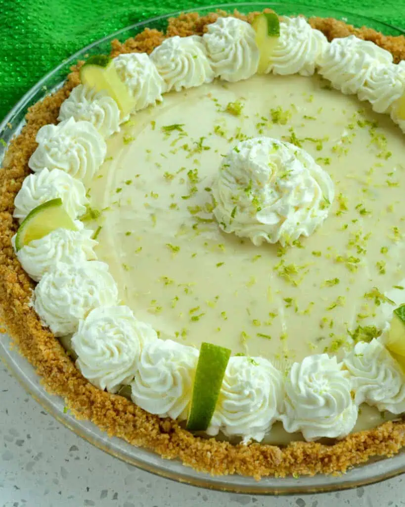 A whole key lime pie decorated wth whipped cream, lime slices, and lime zest. 