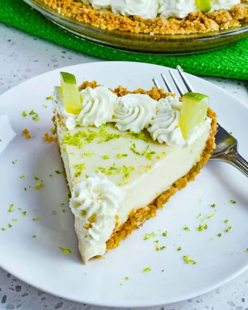 A pierce of key lime pie on a plate with a fork and lime zest. 