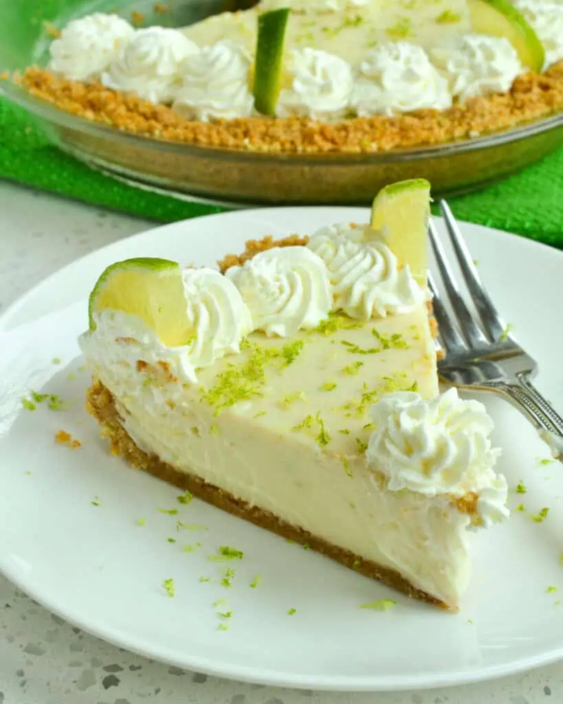 A piece of key lime pie on a plate in front of the pie dish. 