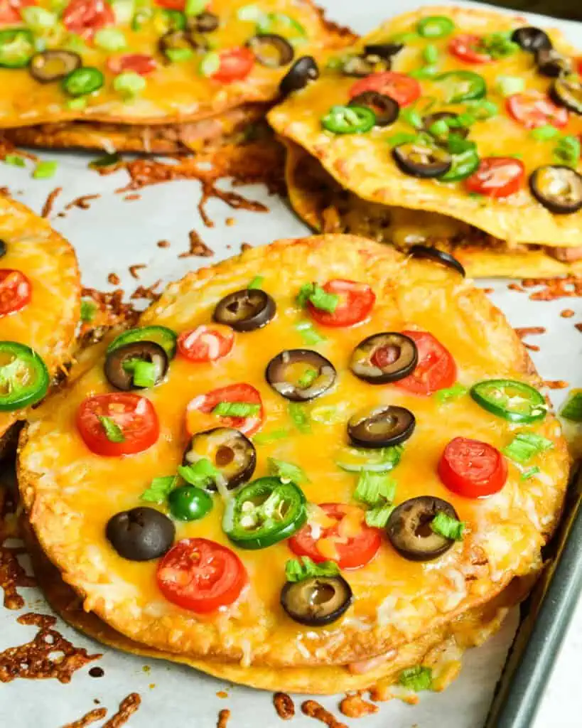 Mexican pizza topped with tomatoes, jalapeno, and black olives, on a baking sheet covered with parchment paper.