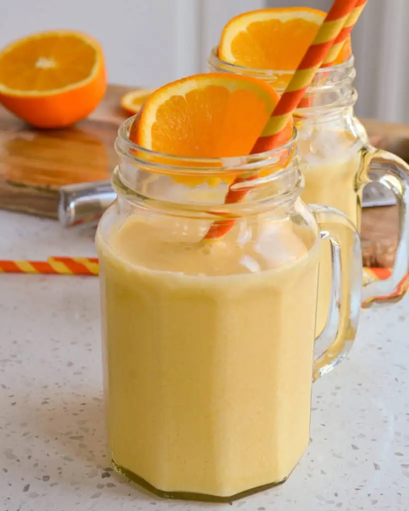 Mugs full of creamy frozen orange julius garnished with orange slices. 