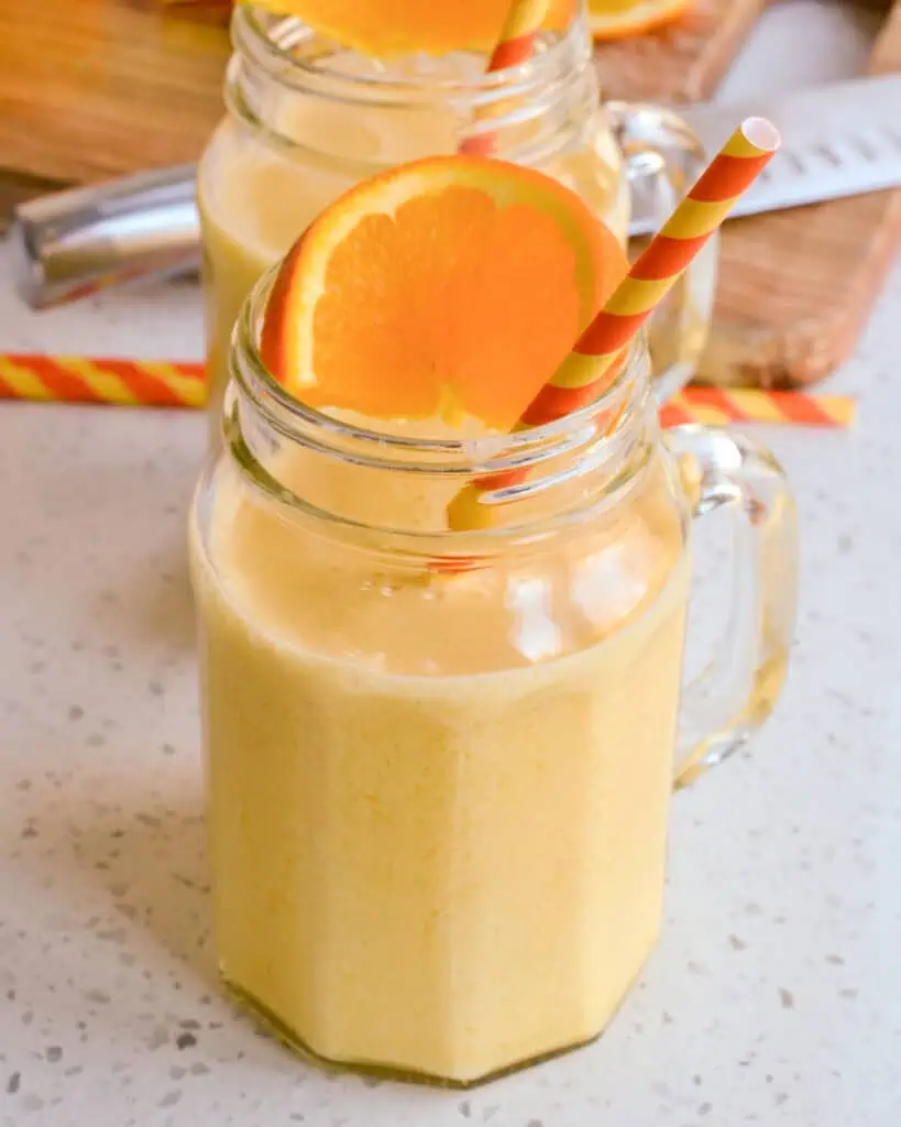 Two glass mugs full of orange julius. 