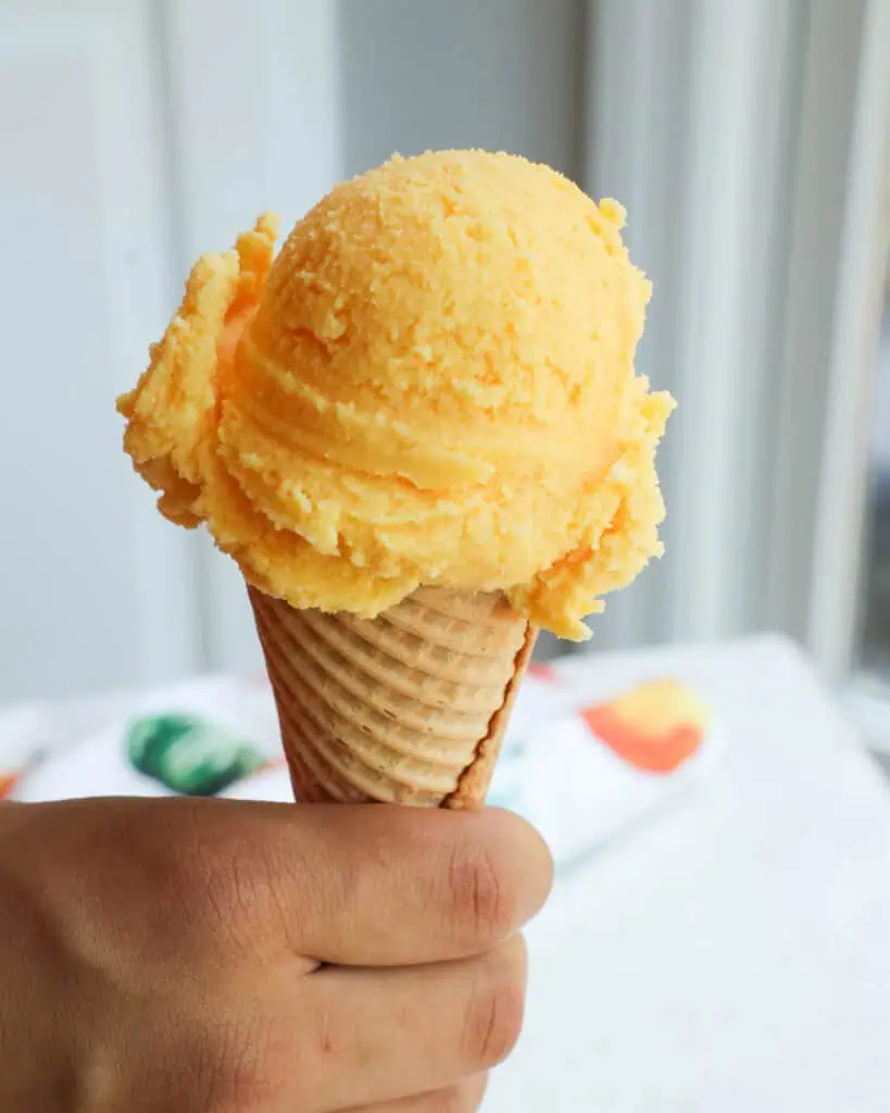 A scoop of orange sherbet on a sugar cone. 