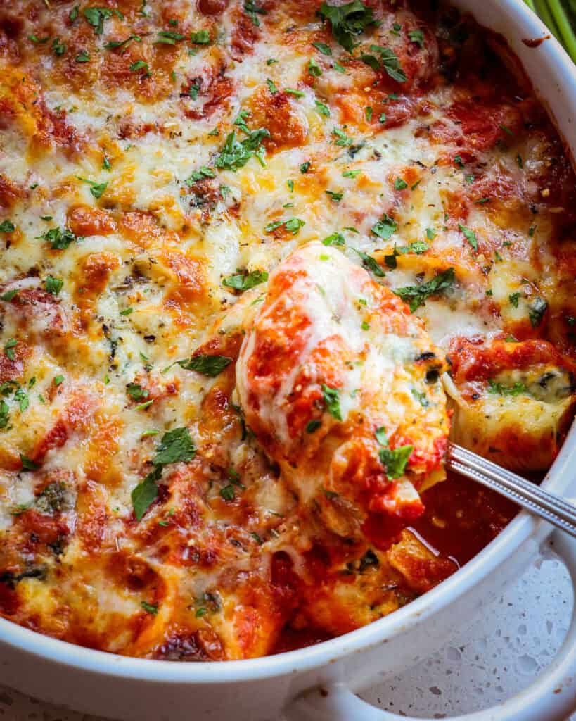 A metl spoon holding a ricotta and spinach stuffed pasta shell.