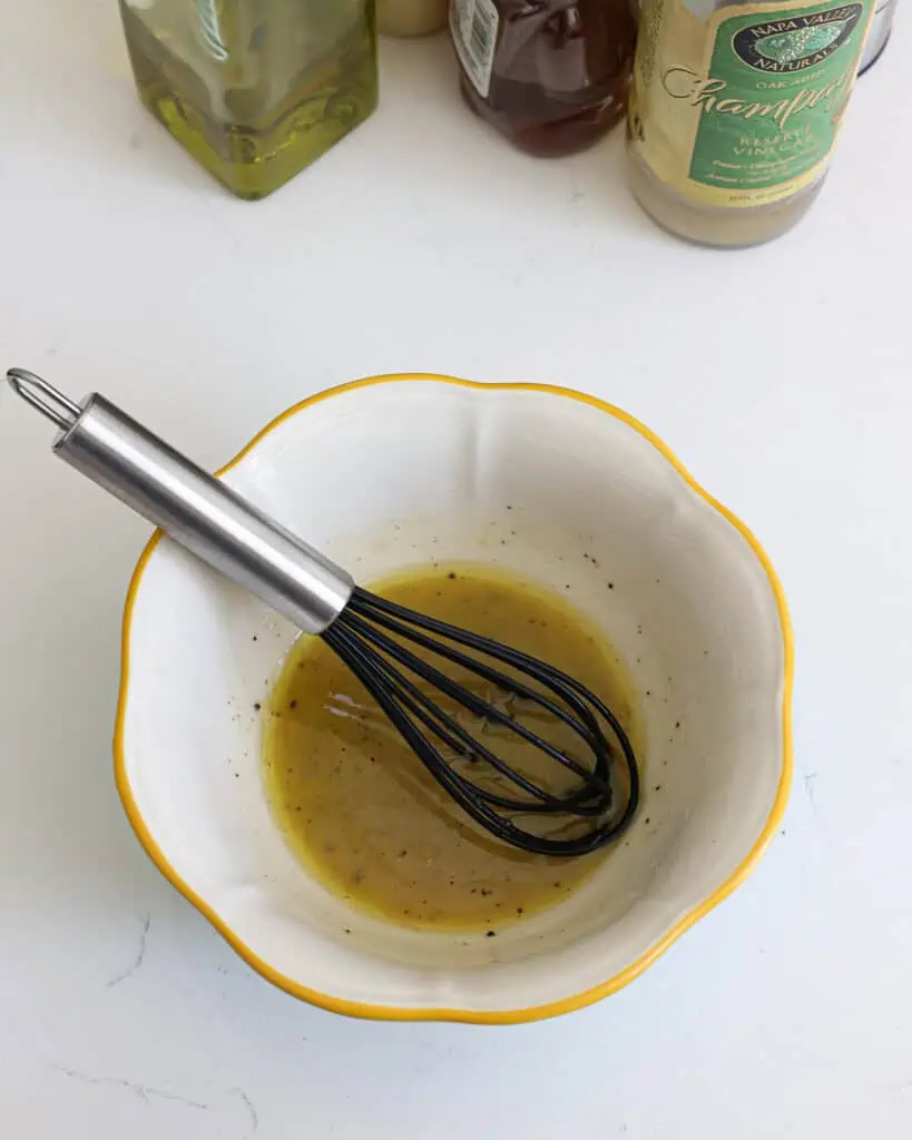 A small bowl with a little bit of mustard vinaigrette and a whisk. 