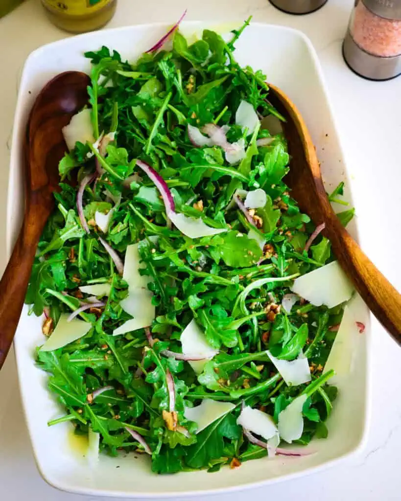 A bowl full of rocket salad with slivered onions, pecans, and shaved parmesan cheese. 