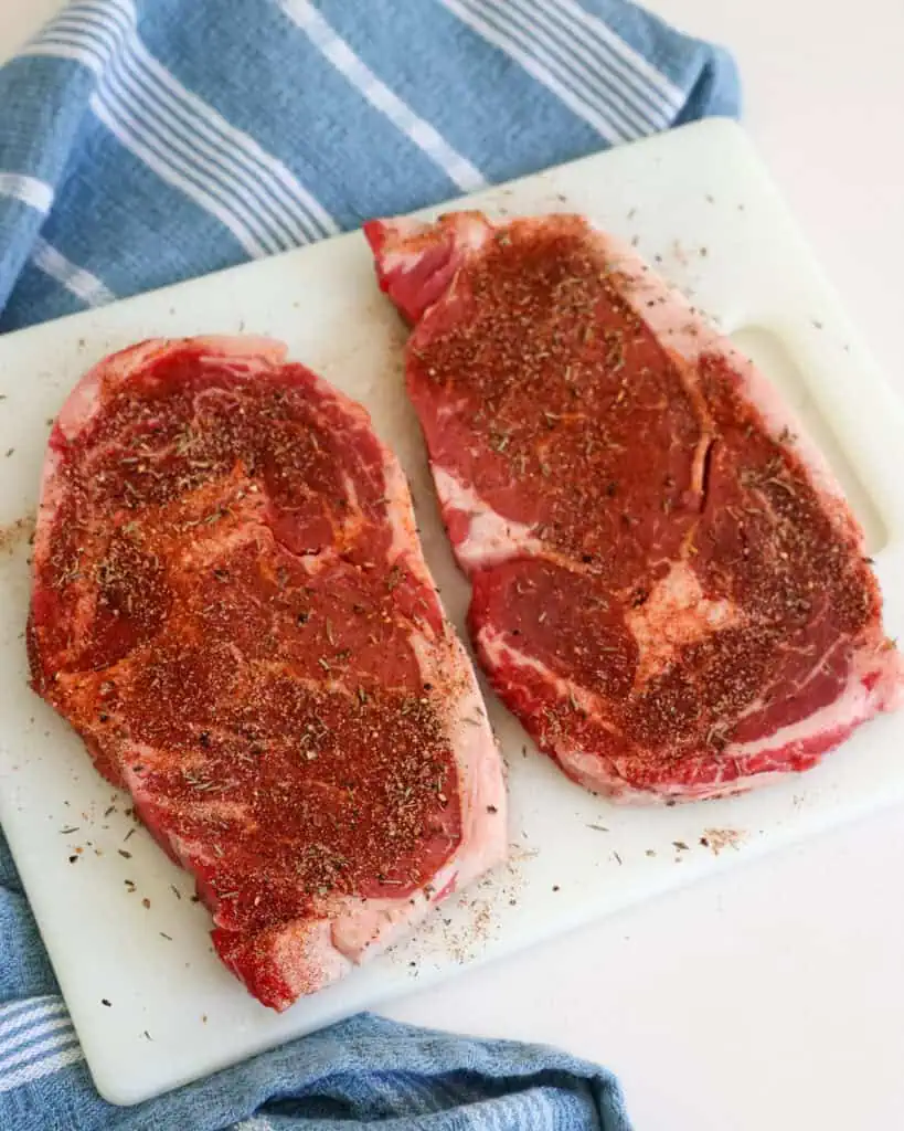 Two ribeye steak with steak seasoning sprinkled over them. 