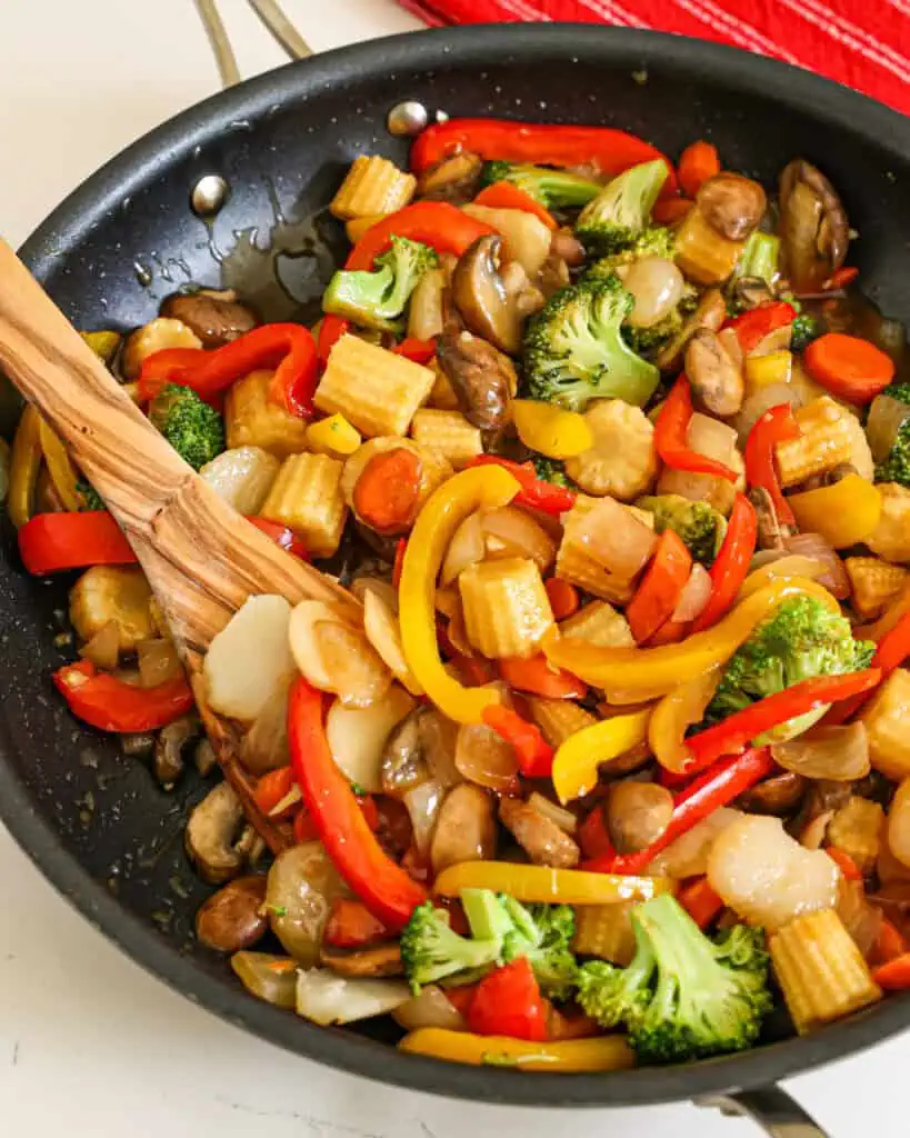 A large skillet full of stir fried vegetables with a wooden spoon in it. 