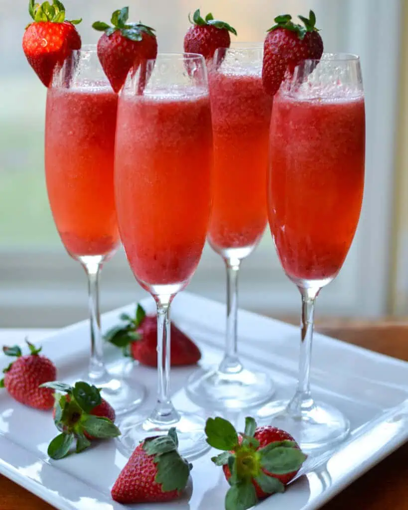 Four strawberry mimosas in champagne flutes garnished with strawberries. 