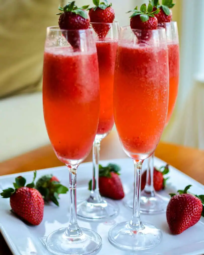 Strawberry mimosas in champagne flutes garnished with fresh strawberries. 