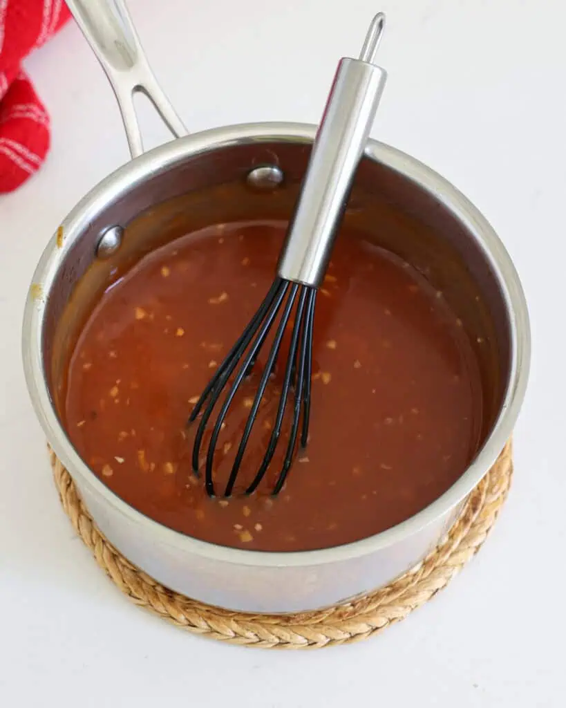 A saucepan full of sweet and sour sauce  with a whisk in it. 