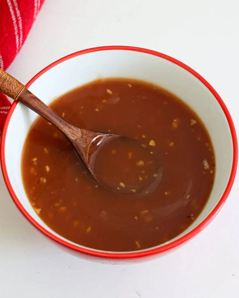A bowl full of sweet and sour sauce with a wooden spoon in it. 