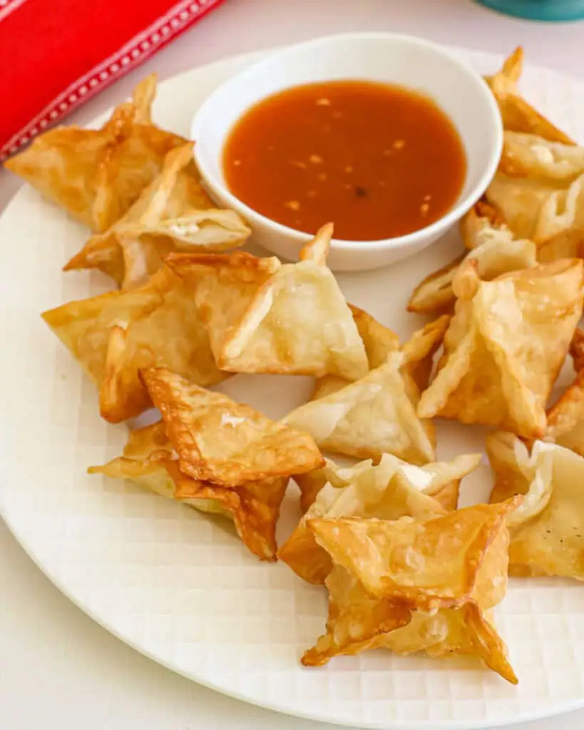 Sweet and sour sauce with cream cheese wontons on a plate. 
