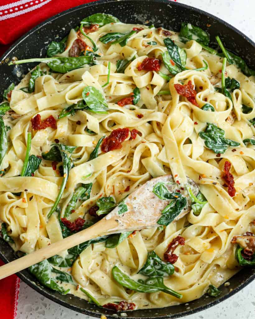 A skillet full of creamy Tuscan Chicken Pasta with golden brown chicken, baby spinach, and sundried tomatoes in a luscious garlic Parmesan cream sauce. 