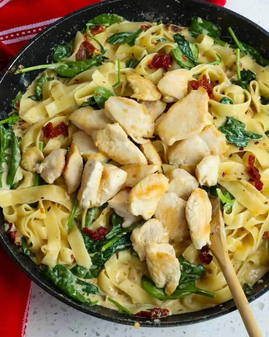 Browned chicken pieces on top of pasta with spinach and sundried tomatoes in a cream sauce. 