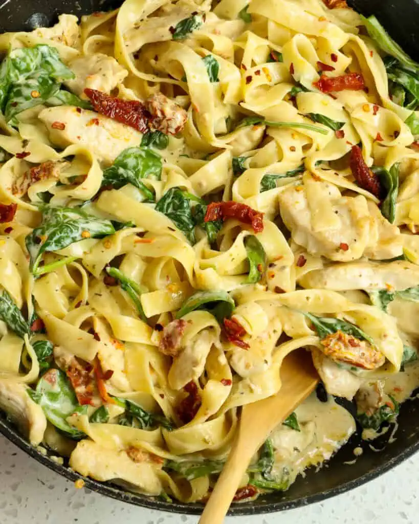 A big pan full of Tuscan chicken pasta with sundried tomatoes and spinach. 