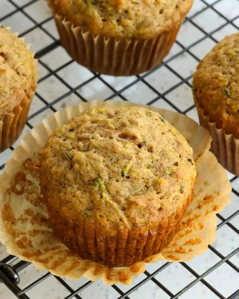 A zucchini muffin with the baking cup removed on a cooling rack. 