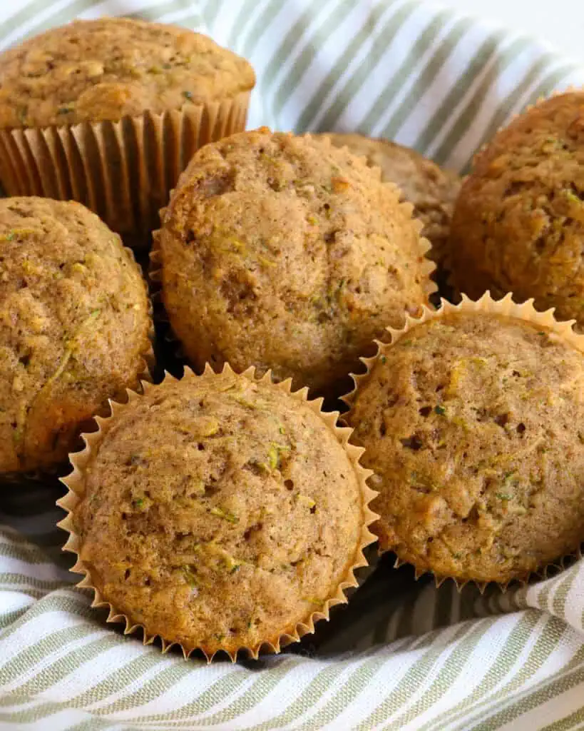 A basket full of zucchini muffins with fresh zucchini and chopped pecans. 