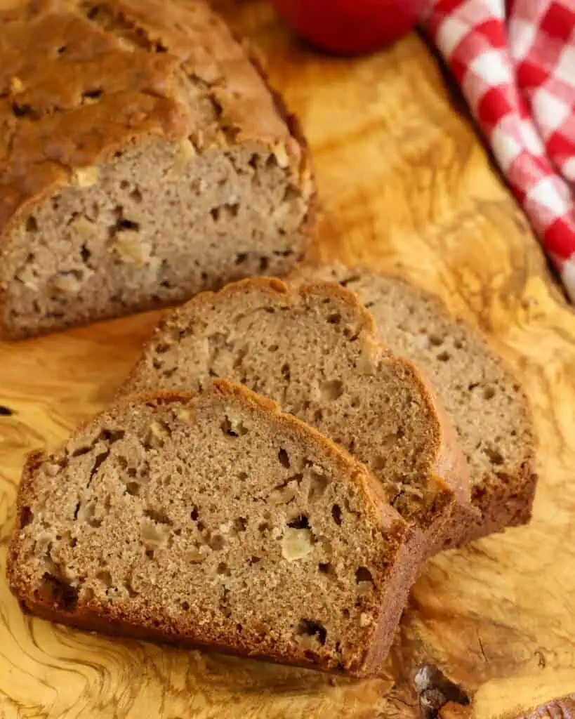 A close up view of three slices of apple bread on a serving board with a red and white checkered towel in the background. 