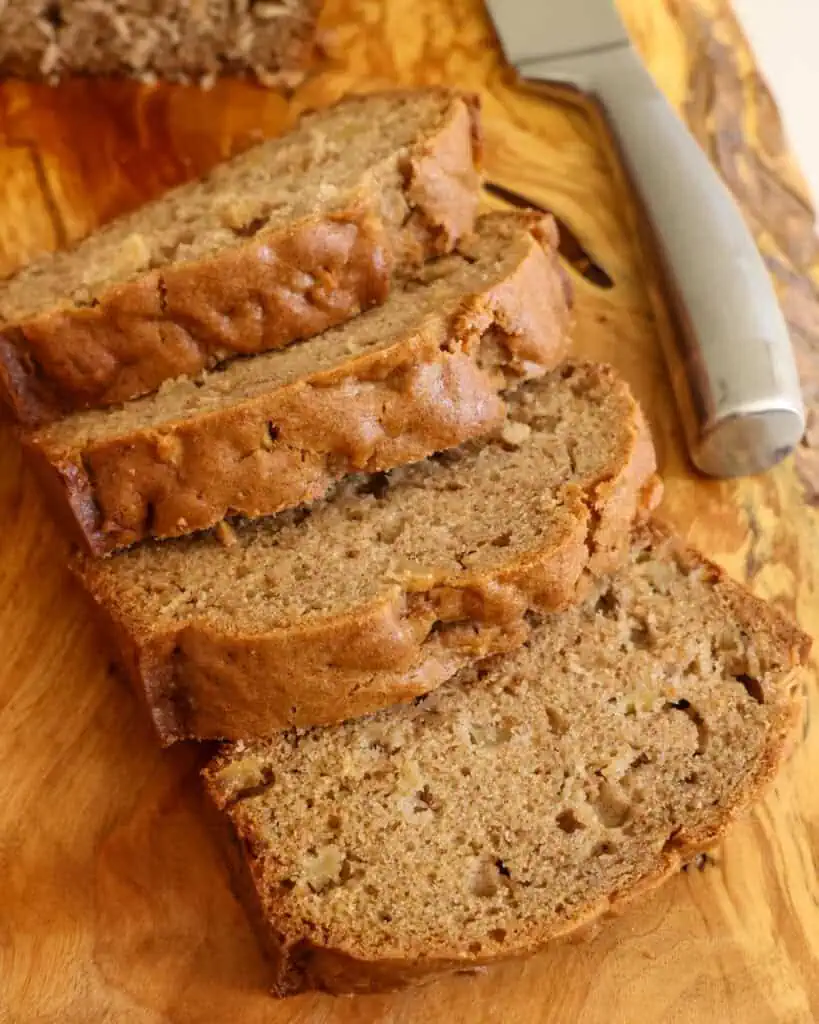 Four slices of apple bread on a serving board with a sharp knife.