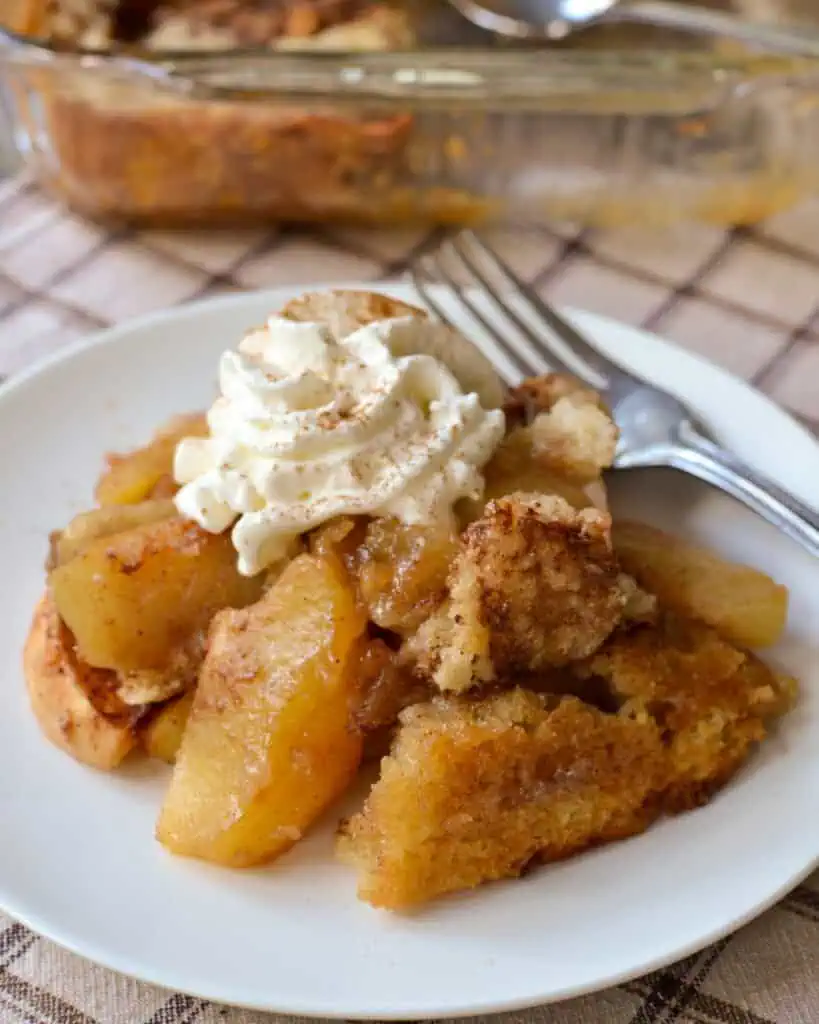 A plate full of apple cobbler with whipped cream on the top. 