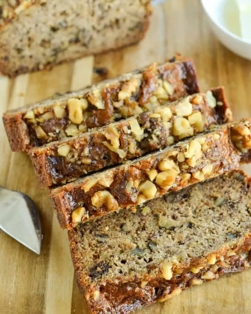 Banana bread slices on a cutting board with a glass bowl of butter pats